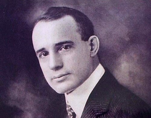 Retrato fotográfico de Napoleon Hill (1883–1970), autor americano e pioneiro da literatura de autodesenvolvimento, com expressão confiante e determinada, terno escuro e gravata, foto em preto e branco típica do início do século XX